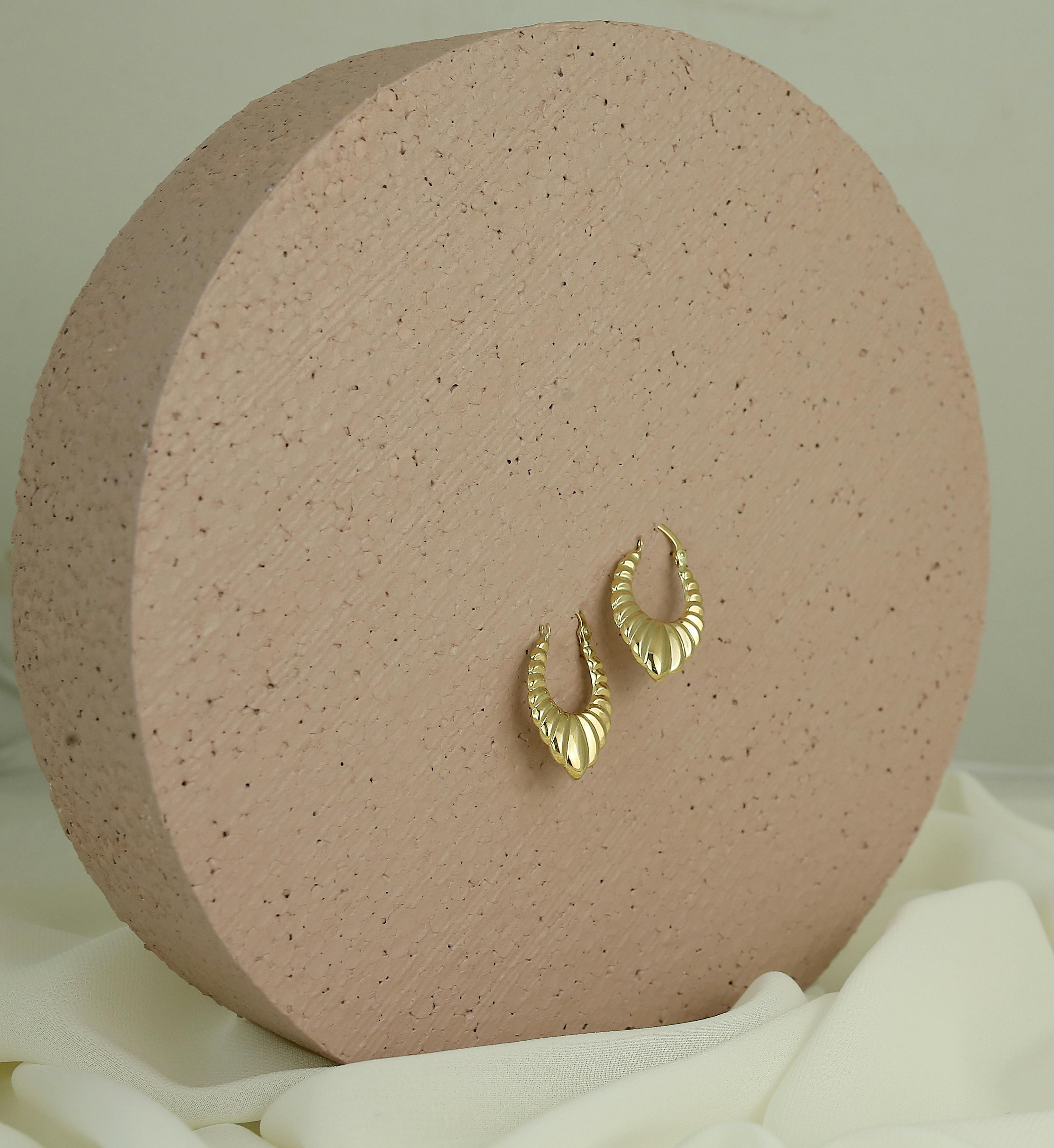Stylish gold shell-shaped earrings elegantly displayed on a textured round stand against a soft background.