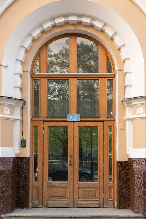 Free A classic wooden entrance with arched design and glass panels, capturing reflections of nature. Stock Photo