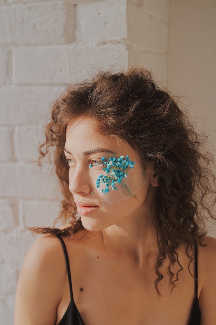 A Woman With Blue Flowers Taped On Her Cheek