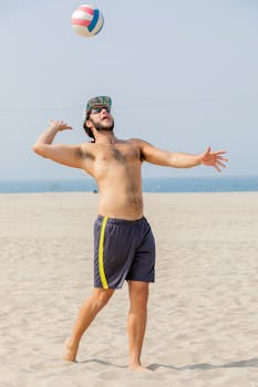 A man playing beach volleyball serves the ball on a sunny day.