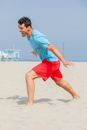 Man in Blue Polo Shirt and Red Shorts Running on White Sand