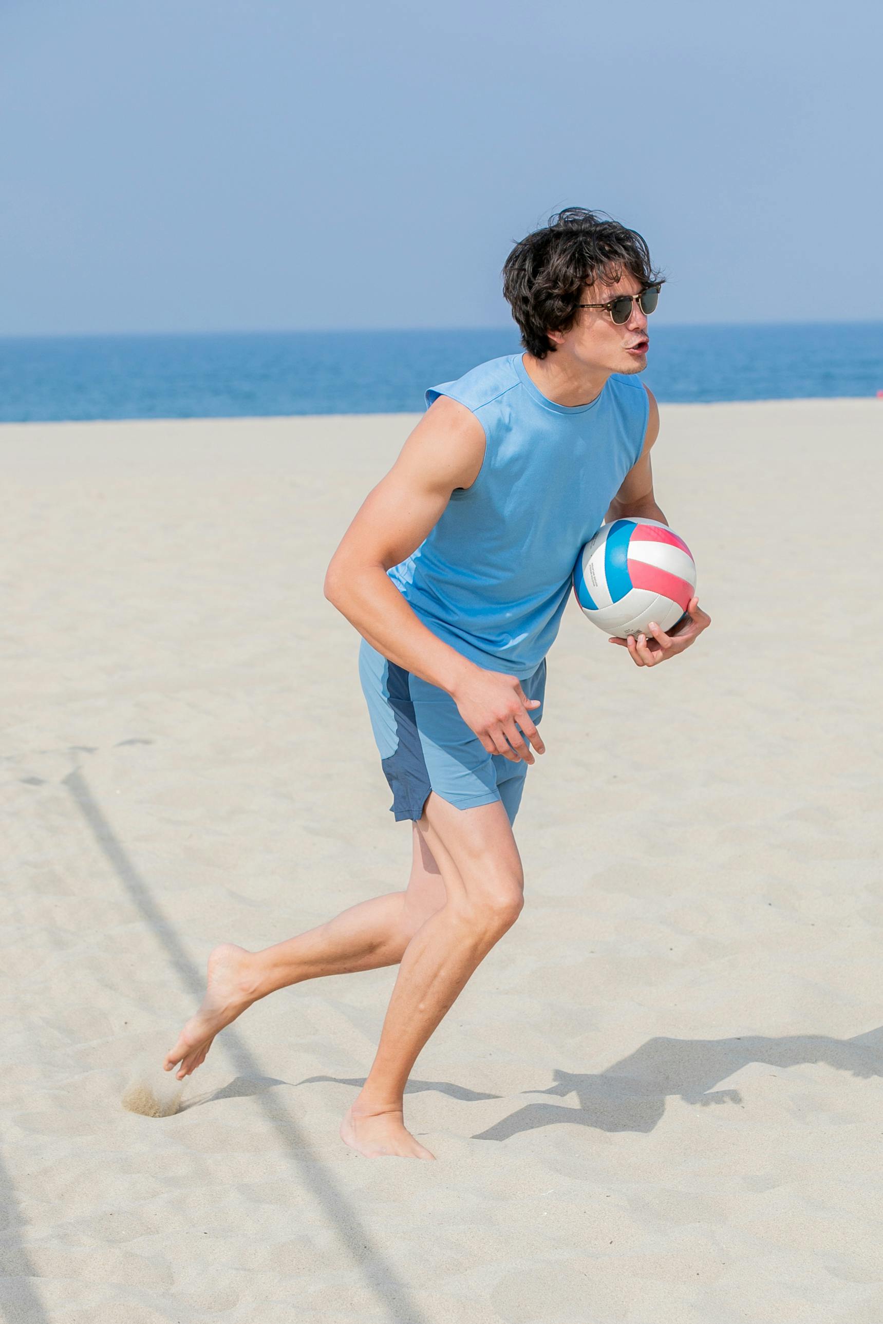 man running on a beach holding a volleyball