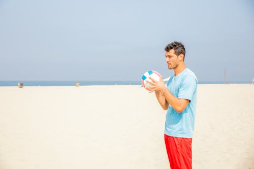 Man Standing on Sandy Beach Preparing for Serving Ball