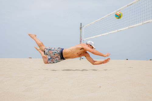 Free Athletic man dives midair to hit volleyball on a sunny beach day. Stock Photo