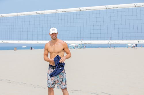 Free Young Smiling Man on Beach with Volleyball Net in Background Stock Photo