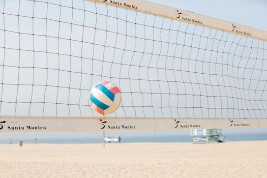 Colorful volleyball in mid-air at Santa Monica beach with net in foreground.