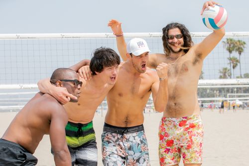 Free Four men celebrating a volleyball victory on a sunny beach day. Stock Photo