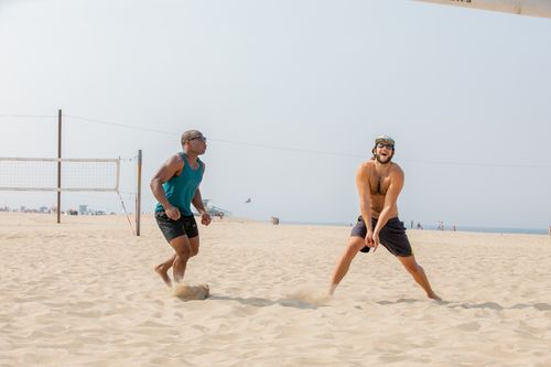 Free Two men intensely playing beach volleyball on a sunny day with sand and sea in the background. Stock Photo
