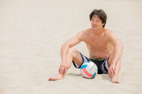 Free Young Handsome Man Sitting on Sandy Beach with Ball Stock Photo