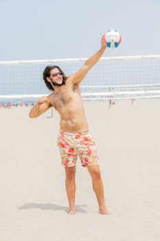A man in colorful shorts enjoying a game of beach volleyball under clear skies.
