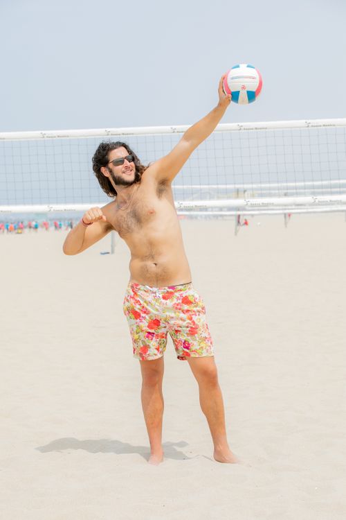Free A man in colorful shorts enjoying a game of beach volleyball under clear skies. Stock Photo
