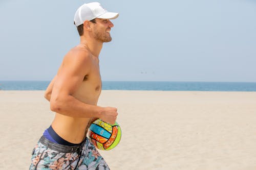 Man in Swimming Trunks and a Cap Running with a Ball