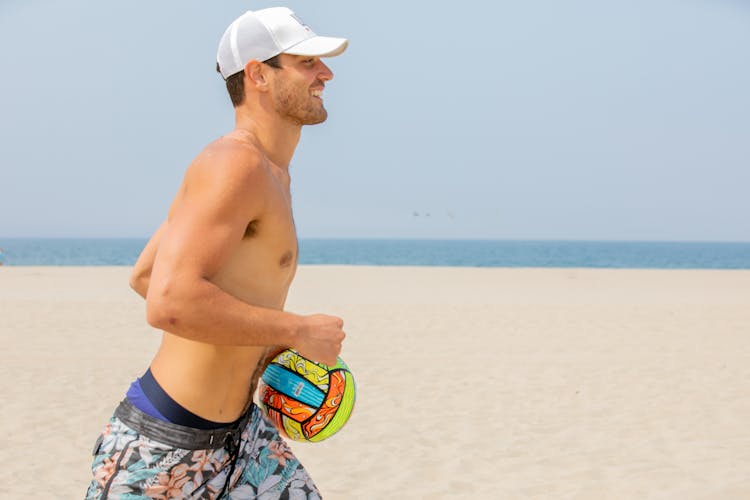 Man In Swimming Trunks And A Cap Running With A Ball