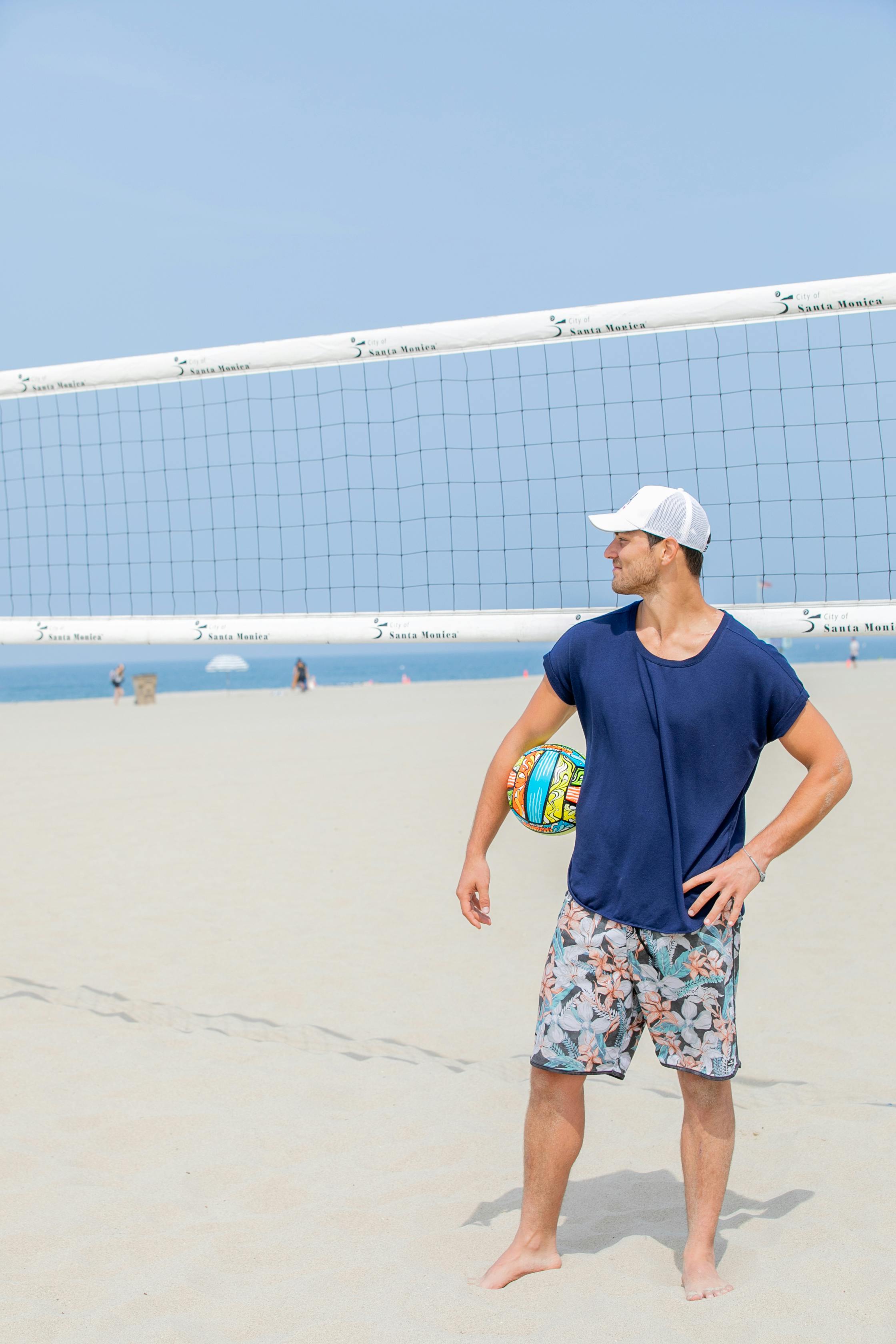 man holding a volleyball ball and standing next to a net on a beach