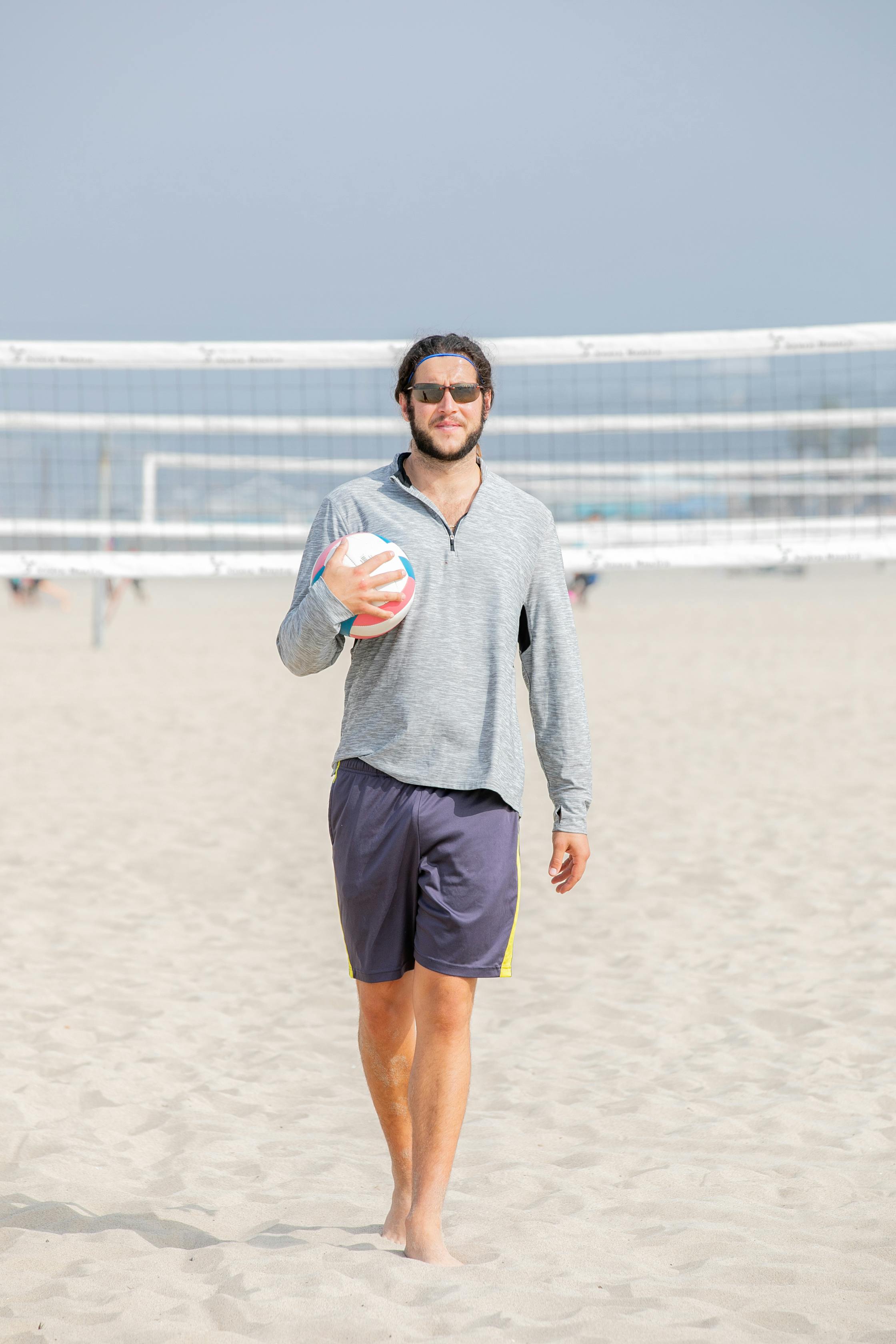 young bearded man walking on beach with ball in hand