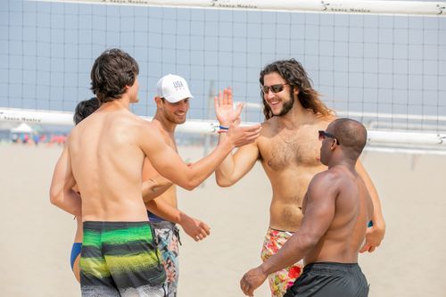 Free Young adults enjoying a lively beach volleyball game with high fives and smiles. Stock Photo