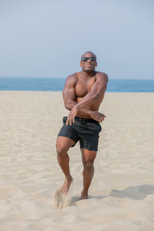 Free Shirtless man dancing energetically on a sunny beach, showcasing fun and vitality. Stock Photo