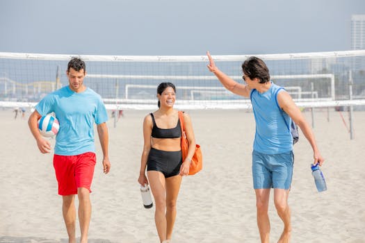 Three friends laughing and walking on a sunny beach after a volleyball game.