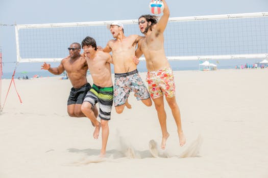 Young friends joyfully playing volleyball on the beach, jumping and celebrating.