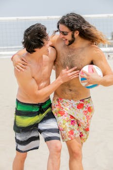 Two friends enjoying a game of volleyball on a sunny beach, embracing and smiling.