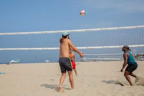 Free Group of friends playing beach volleyball under sunny skies. Perfect for summer fun themes. Stock Photo