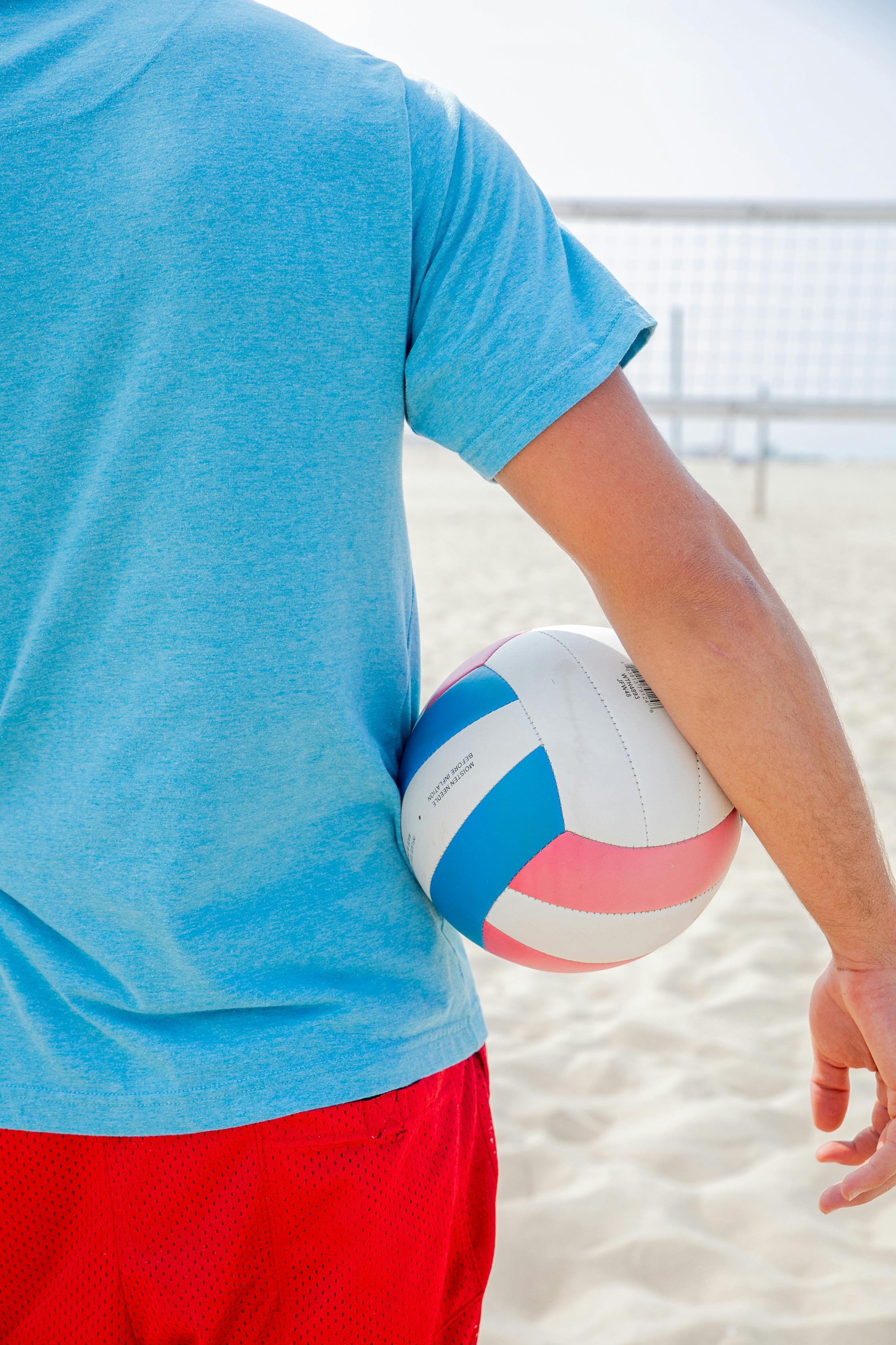 man holding a volleyball ball on a beach volleyball court