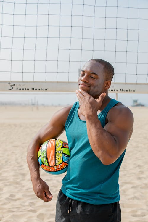 Man Smearing Sunscreen on His Face on a Beach and Holding a Volleyball Ball