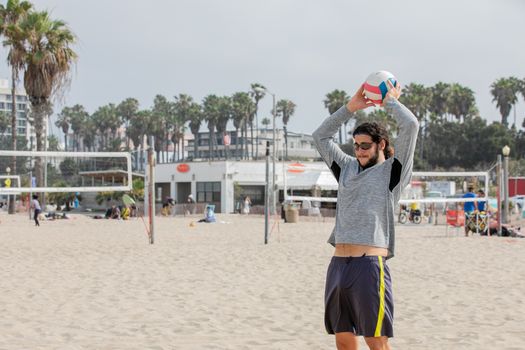Man playing volleyball on a sunny beach with palm trees and volleyball net in the background