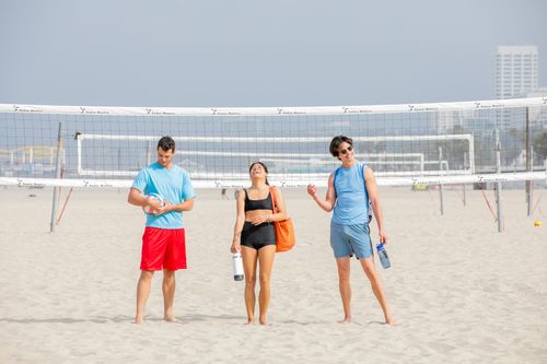 Free Three friends laughing on a sunny beach volleyball court, enjoying summer fun and friendship. Stock Photo