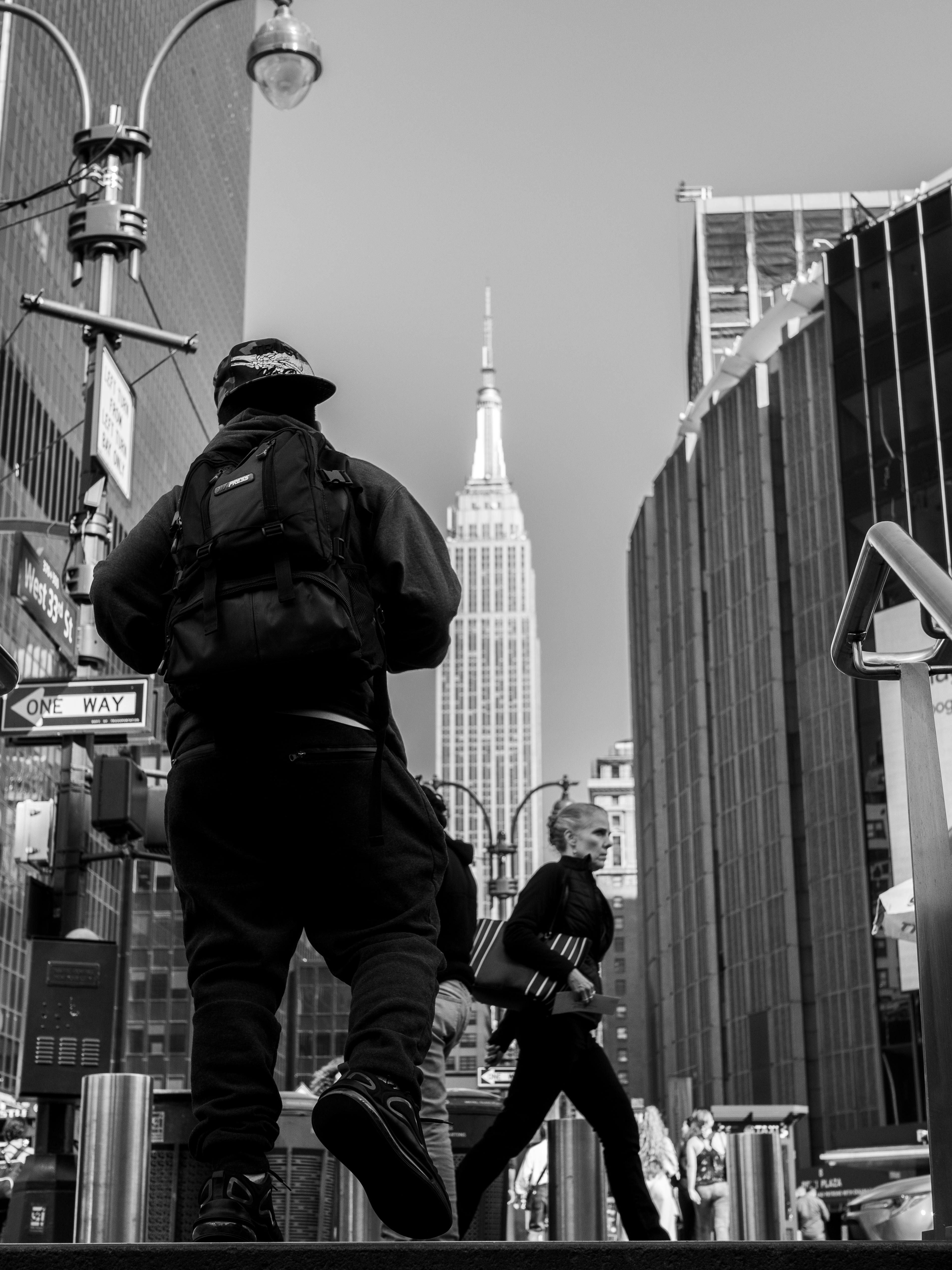 Black-and-white photo of people walking on a city street with a famous skyscraper in the background.