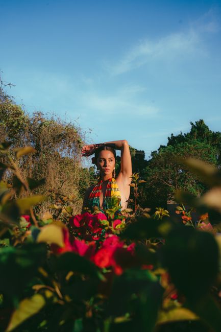 A woman poses in a colorful flower field under a clear blue sky, showcasing nature's beauty.