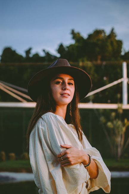 A fashionable woman wearing a hat poses elegantly outdoors during a sunset in Zapopan, Mexico.