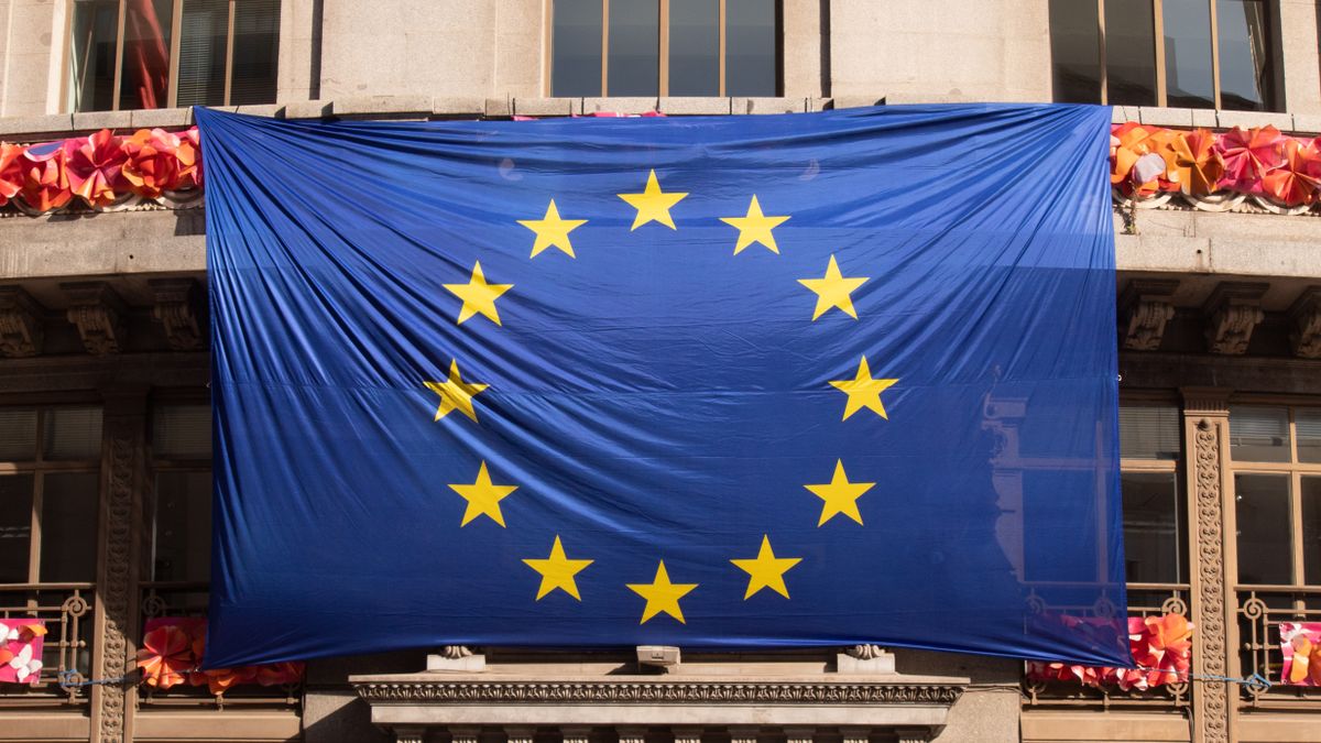 Large European Union flag draped over a building facade adorned with festive decorations.