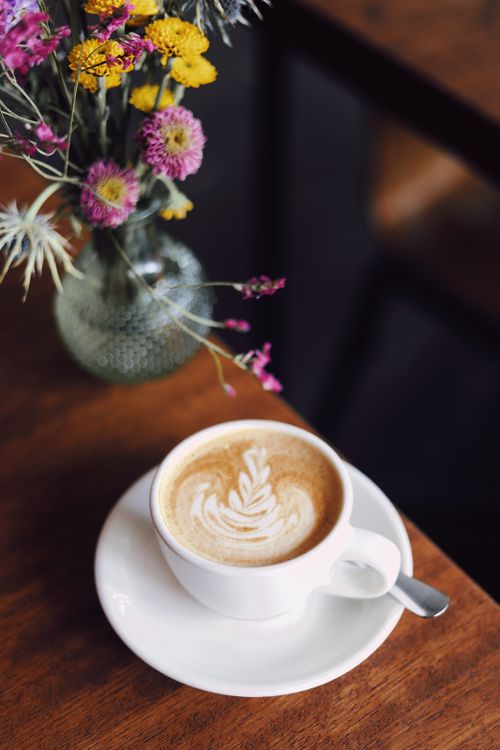 Free Beautiful latte art beside a vibrant floral arrangement in a Berlin café setting. Stock Photo