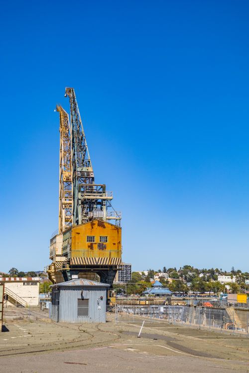 Free A towering crane stands in a shipyard, silhouetted against a vivid blue sky, showcasing industrial might. Stock Photo