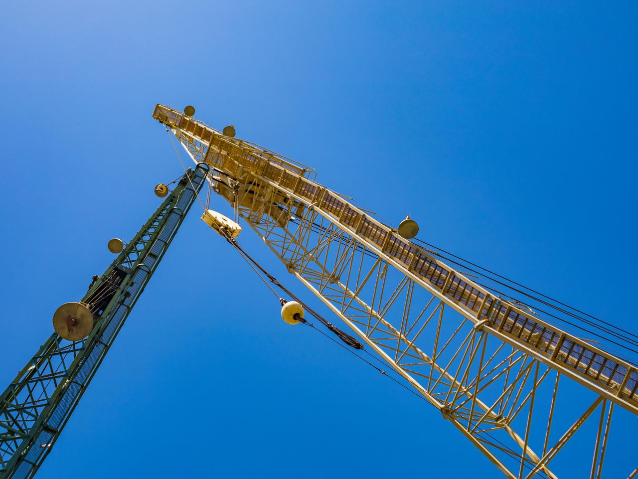 Low-angle view of two construction cranes against a clear blue sky.
