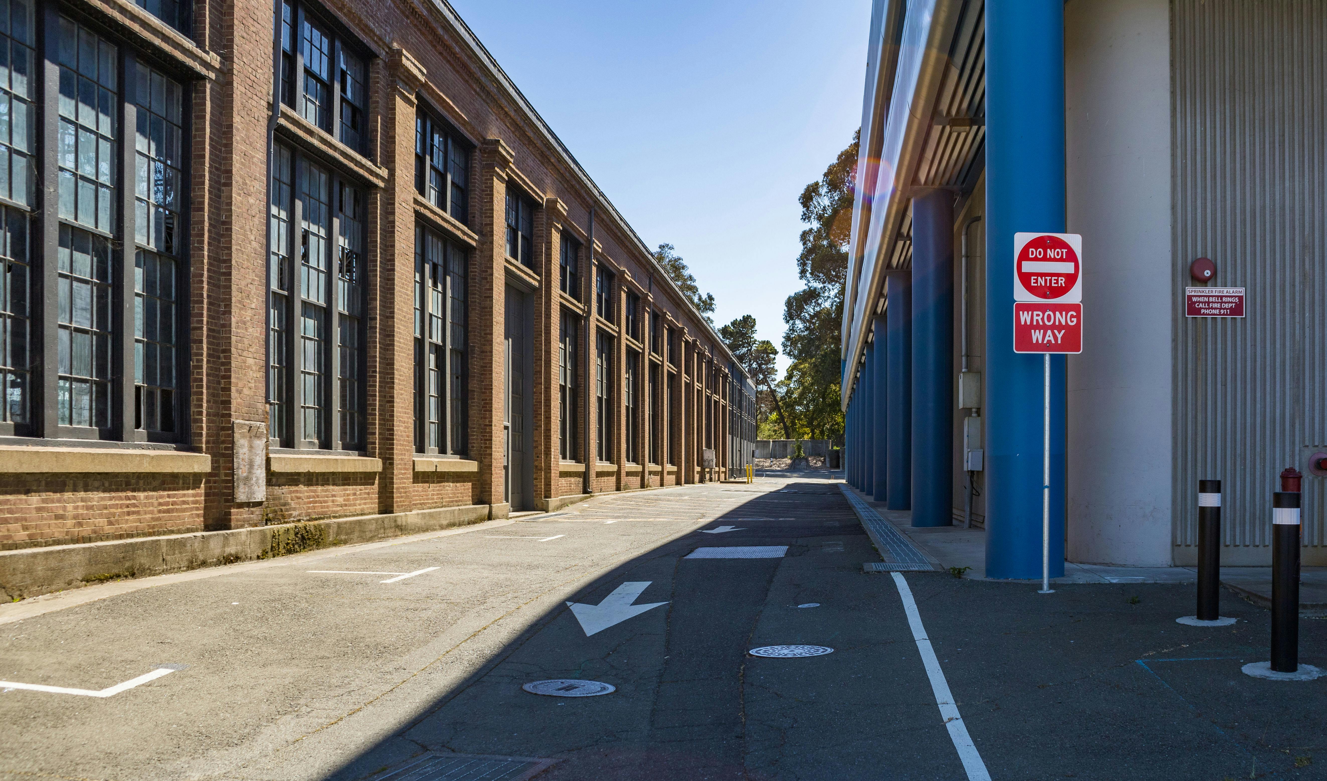 Exterior of a large industrial building with 'Do Not Enter' and 'Wrong Way' signs on a sunny day.
