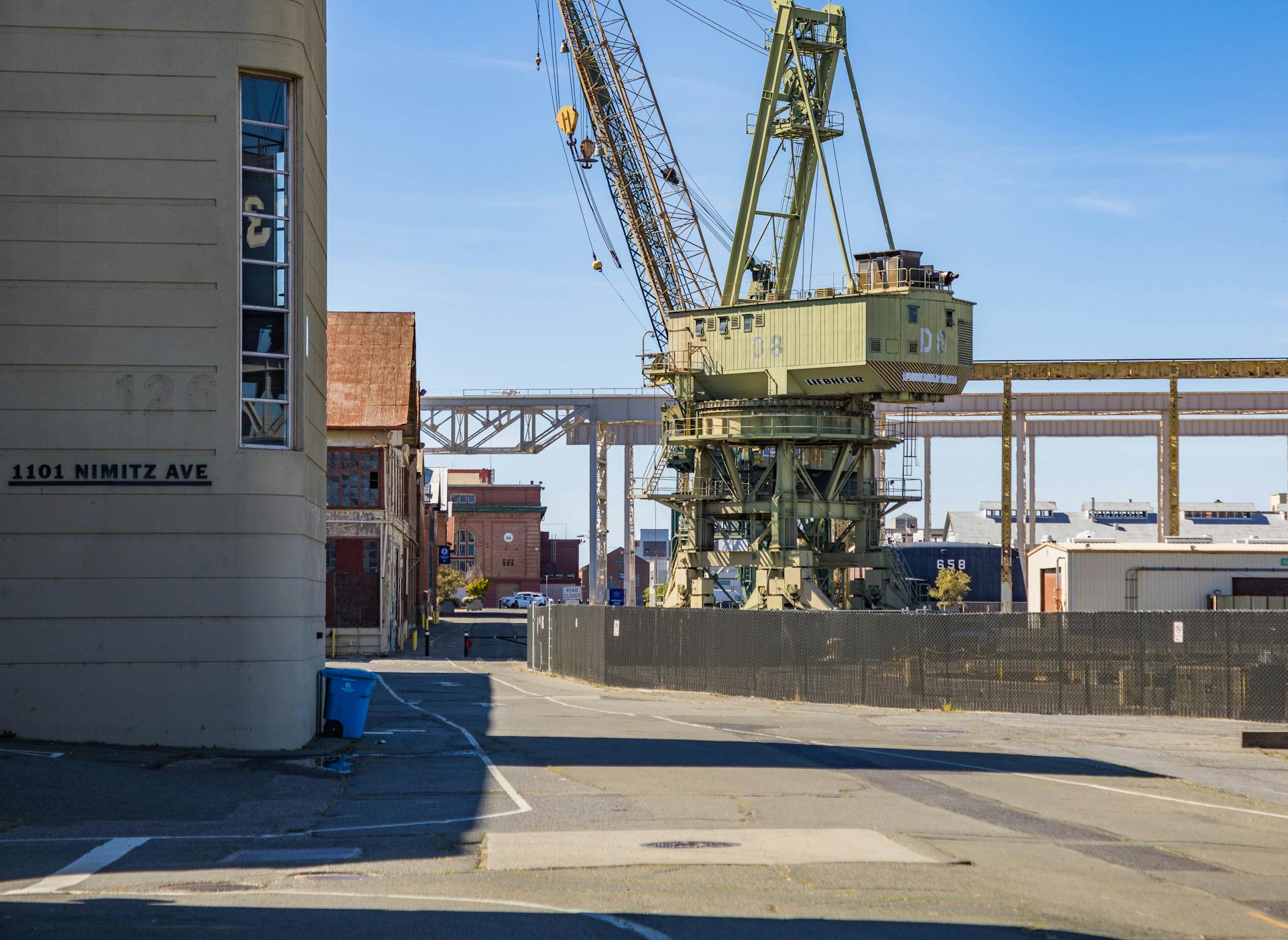 An industrial harbor scene featuring a large crane beside warehouses and a pier under clear skies.