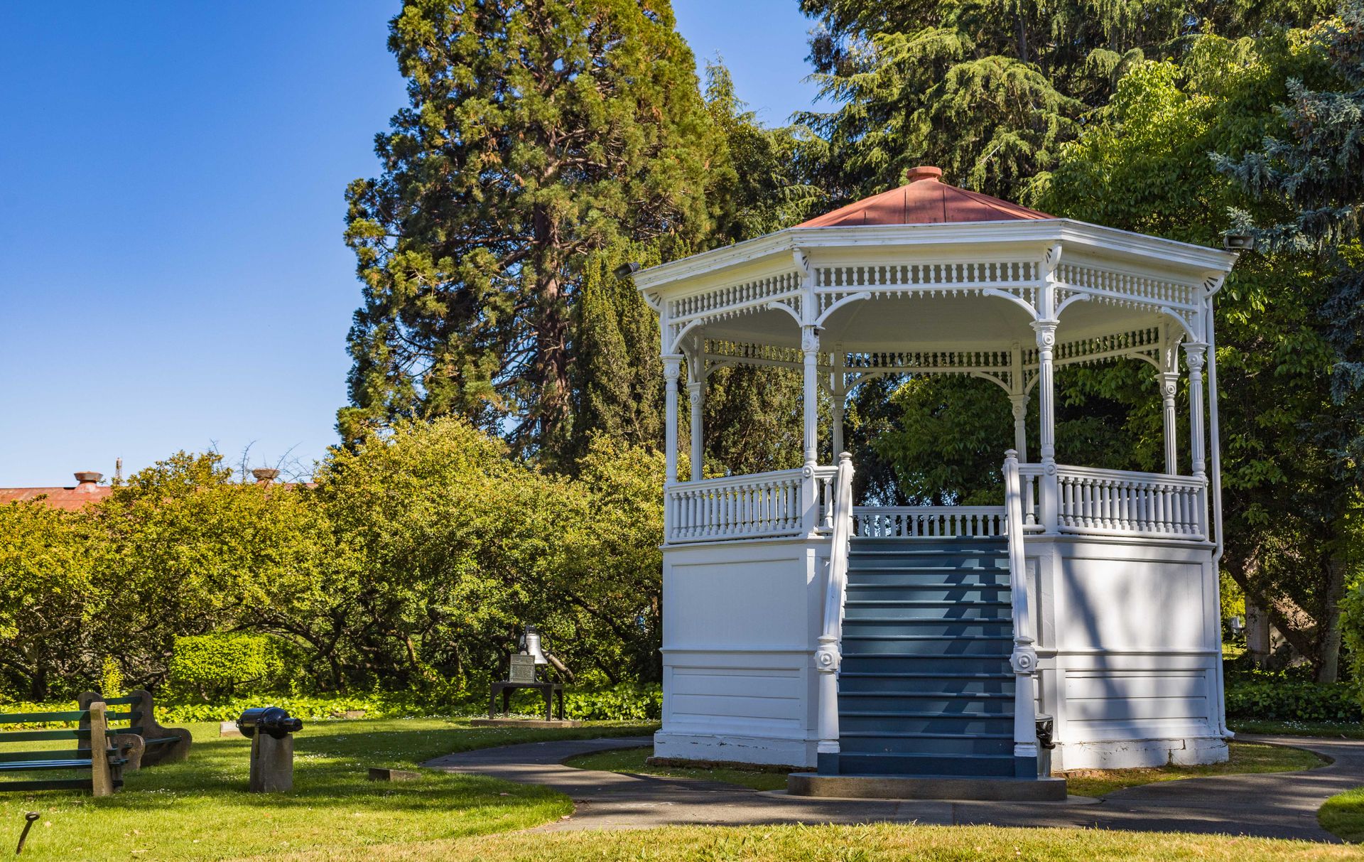 A picturesque white gazebo surrounded by lush greenery and blue sky in a tranquil park.
