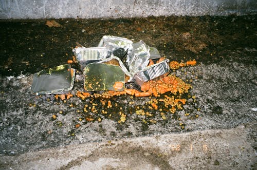 Imagen de Alimentos Desperdiciados en Envases de Aluminio en el Suelo