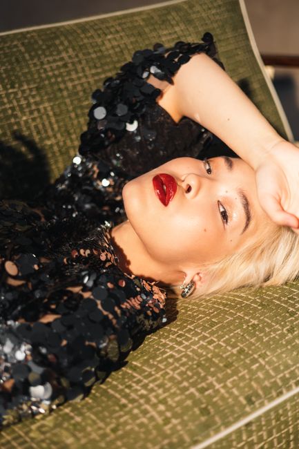 Glamorous woman posing with red lipstick in a sequin dress on a vintage sofa.