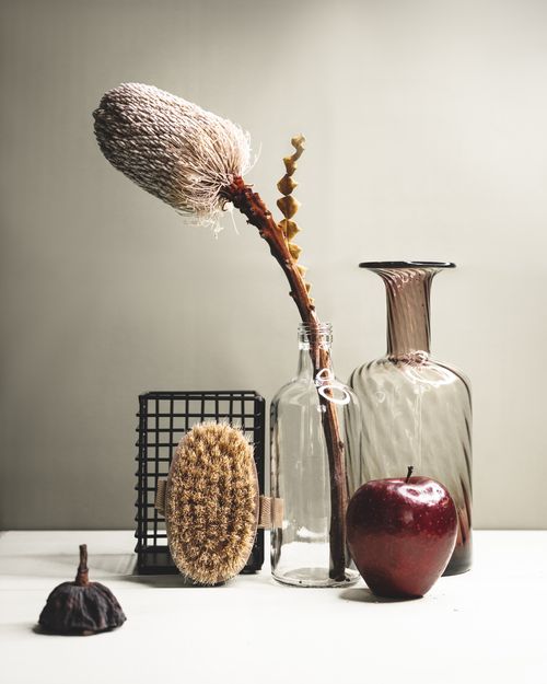 Free A rustic still life with natural elements: dried flower, apple, glass vases, and brush for home decor. Stock Photo