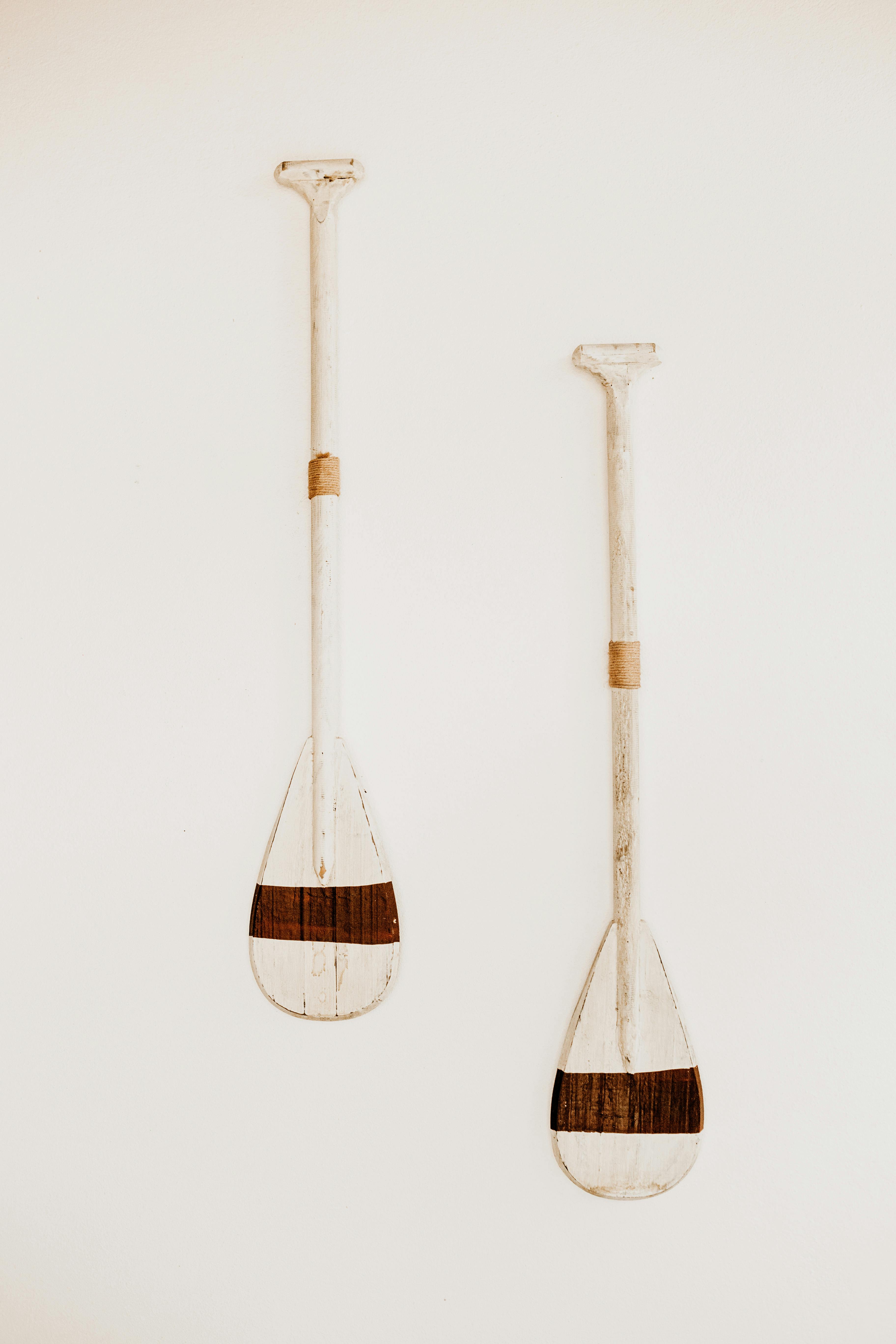 A minimalist still life featuring two rustic wooden canoe paddles against a stark white background.