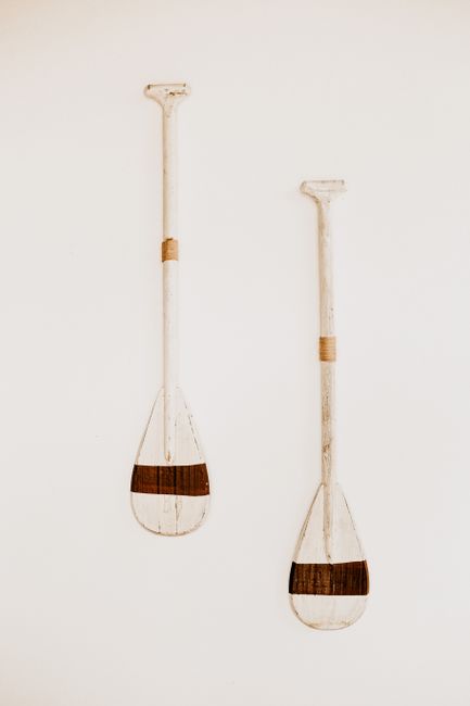 A minimalist still life featuring two rustic wooden canoe paddles against a stark white background.