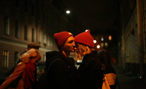 Мужчина целует нос женщины на улице в ночное время