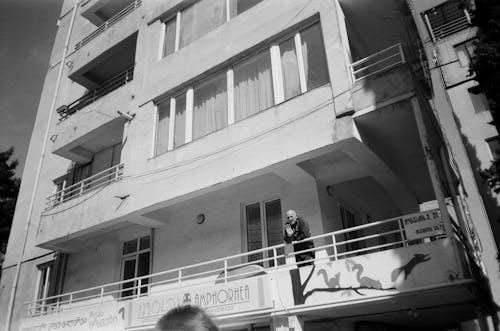 Greyscale Photo of Man Waving at Person While on Balcony of a Building