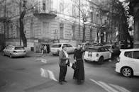 在繁忙的街角，两个成年人正在交谈，周围停满了汽车，画面是单色的