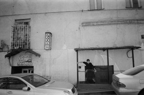 Free A black and white photo of a young man sitting by parked cars on a street. Stock Photo