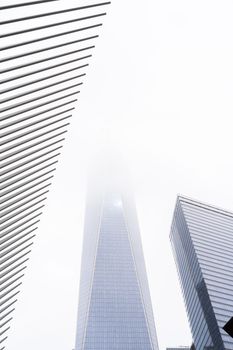 A foggy view of contemporary skyscrapers reaching into the sky, surrounded by urban architecture.