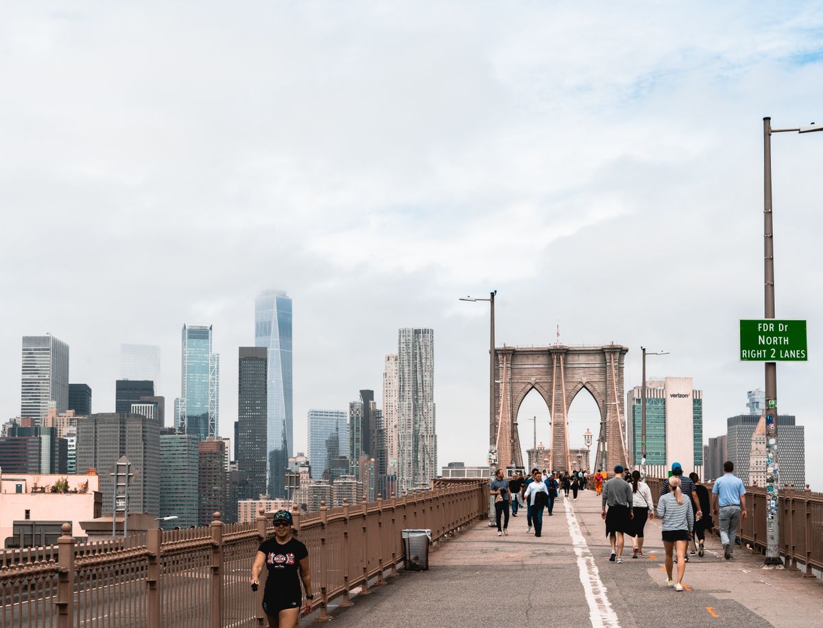 Pedestrians walking the Brooklyn Bridge with the Lower Manhattan skyline behind
